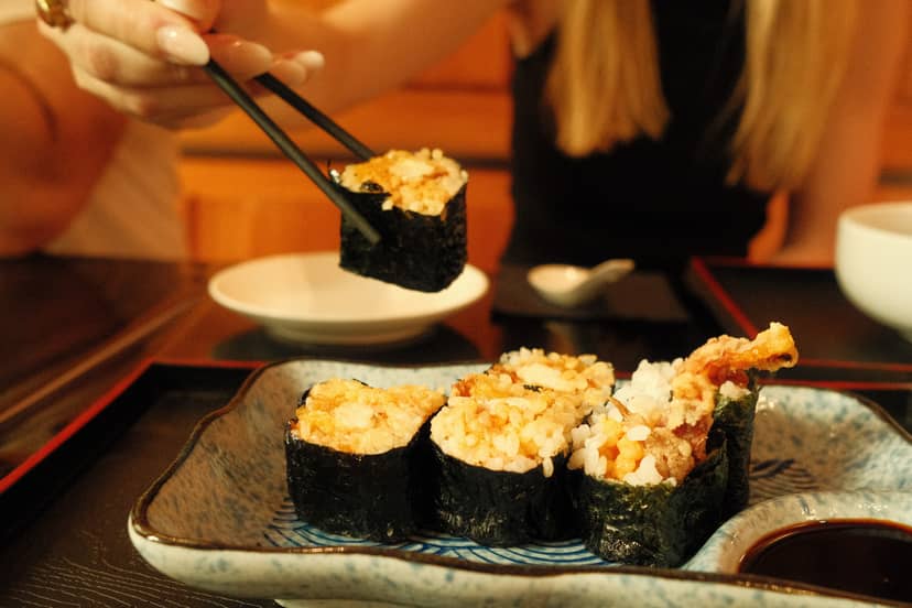 SHOKUDO Izakaya sushi rolls with tempura topping and nori, eaten with chopsticks in Zürich.
