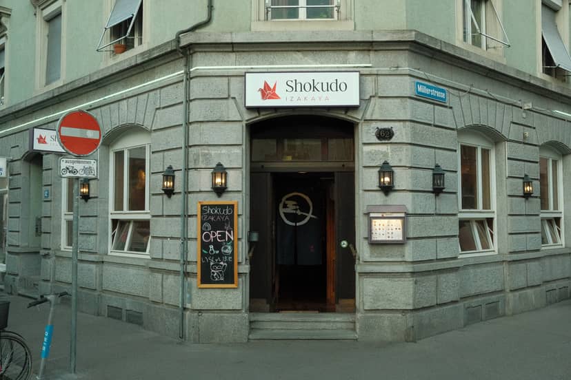 Shokudo Izakaya Japanese restaurant storefront on Zürich street corner with stone facade and illuminated entrance.